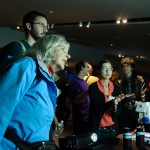 Darcy Taniguchi discusses marine microbes as guests look on at the diminutive creatures darting across the screen. Credit: John Gillooly