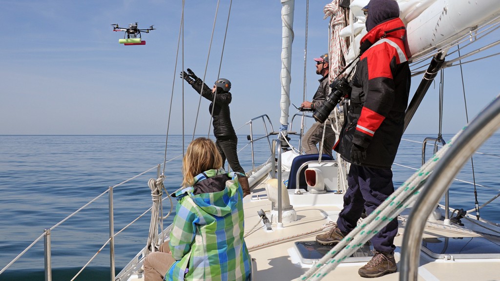 Drones are providing a powerful new tool for whale research and conservation. Here, NOAA’s John Durban (center rear) uses a remote control to guide a hexacopter into the outstretched hands of his NOAA colleague, Holly Fearnbach, as WHOI microbiologist Amy Apprill (seated) and New England Aquarium whale specialist Marilyn Marx look on. Durban makes it look easy, but maneuvering a drone from a rocking sailboat is anything but. (Photo by Véronique LaCapra, Woods Hole Oceanographic Institution)