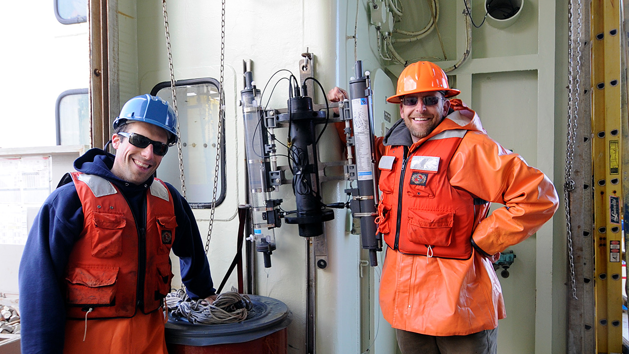 WHOI scientist Benjamin Van Mooy (right) and WHOI-MIT Joint Program graduate student Jamie Collins flank the proof-of-concept version of PHORCYS, the instrument Van Mooy co-developed to make near-real-time measurements of photosynthesis and respiration in the ocean. Previous methods were difficult and time-consuming—PHORCYS yields results much more quickly and easily. Van Mooy and WHOI's Office of Technology Transfer are seeking partners to develop the instrument as a commercial product. (Photo courtesy of Benjamin Van Mooy, Woods Hole Oceanographic Institution)